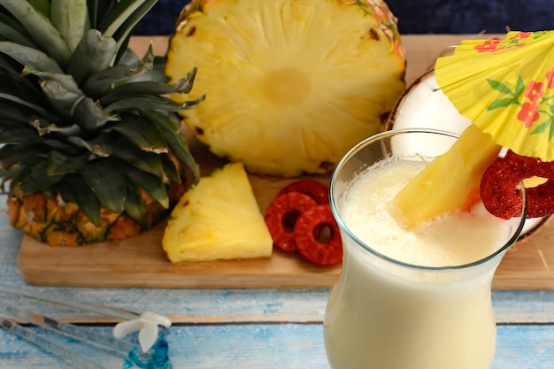 Piña colada con frutas frescas en la tabla de cortar de madera sobre fondo de textura azul