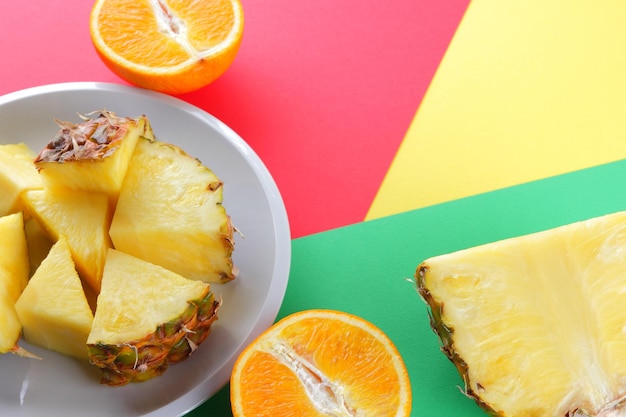 Piña cortada y naranjas en un fondo multicolor Piña y mitades de naranja en un plato blanco