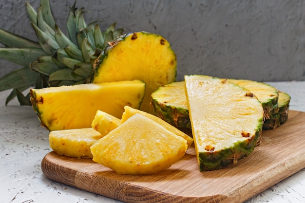 Piña cortada en un tablero de madera en un fondo blanco. Trozos de piña de varios tamaños.