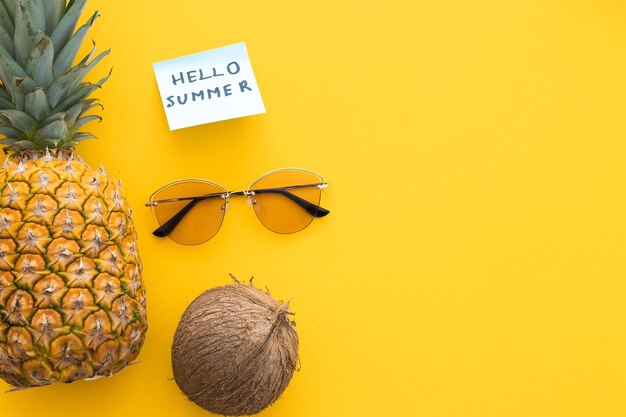 Piña creativa mirando hacia arriba con gafas de sol botella de crema y coco aislado en amarillo