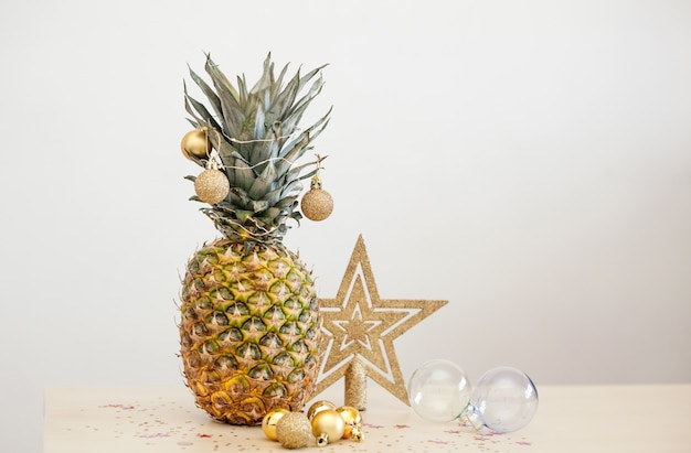 Piña decorada con bolas de Navidad doradas sobre blanco