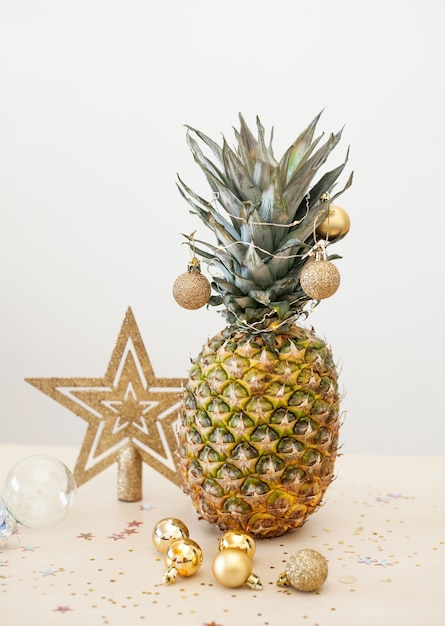 Piña decorada con bolas de Navidad doradas sobre blanco