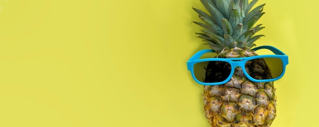 Piña divertida con gafas de sol azules sobre fondo amarillo