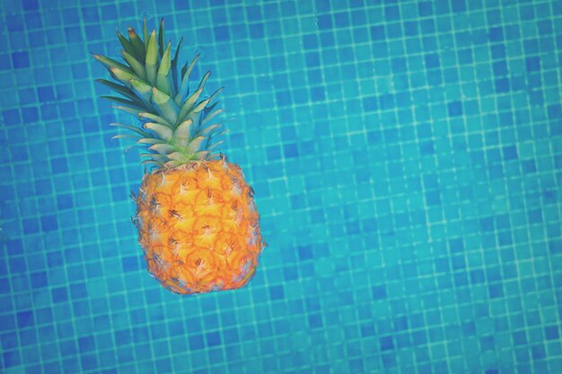 Piña flotando en el agua de la piscina de azulejos, tonos retro