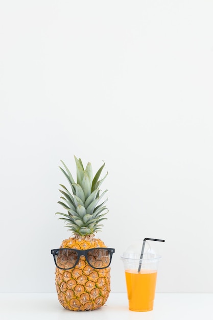 Piña fresca con gafas de sol cerca de un vaso de jugo y una pajita de cóctel sobre fondo de color