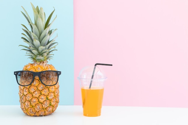 Piña fresca con gafas de sol cerca de un vaso de jugo y una pajita de cóctel sobre fondo de color