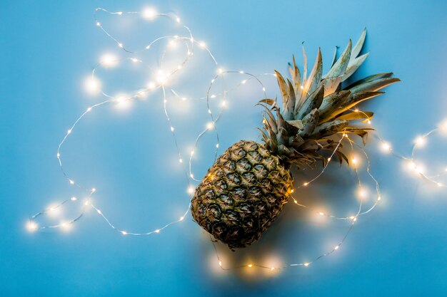 Piña fresca con luces de hadas sobre fondo azul.