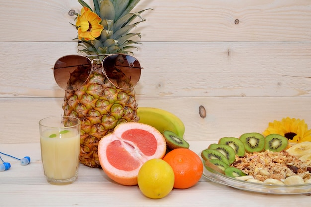 Piña en gafas de sol y frutas tropicales sobre fondo de madera