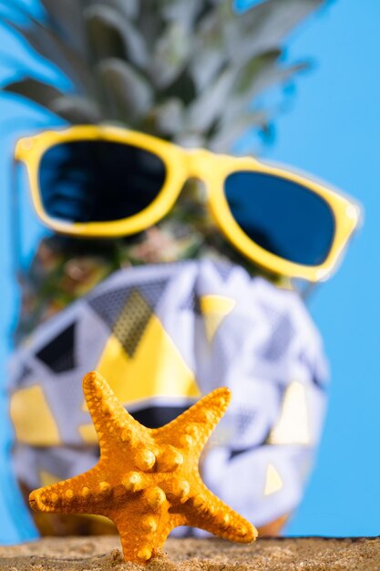La piña en gafas de sol y una máscara protectora se encuentra en la playa de arena
