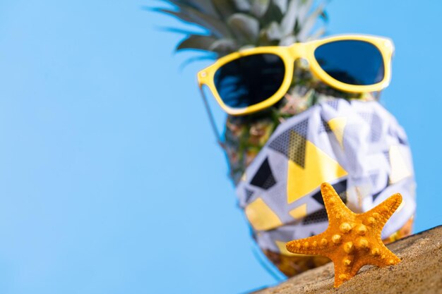 La piña en gafas de sol y una máscara protectora se encuentra en la playa de arena
