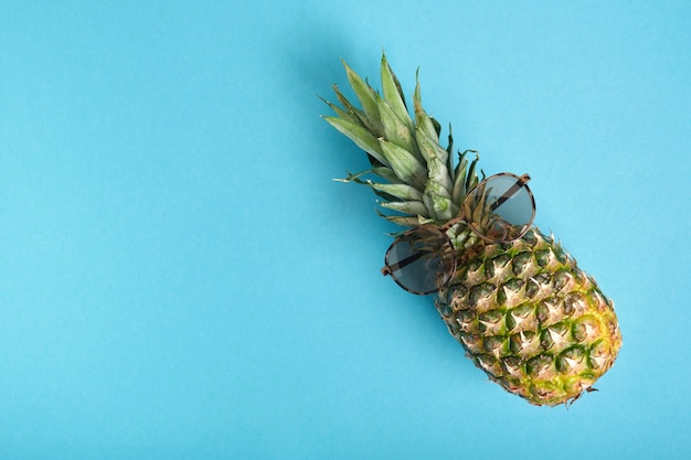 Piña con gafas de sol sobre un fondo azul con espacio de copia