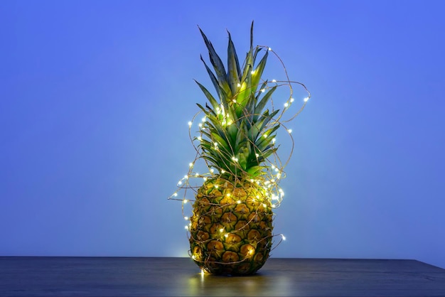 Piña con guirnalda de luces LED de Navidad en el espacio de copia de la mesa