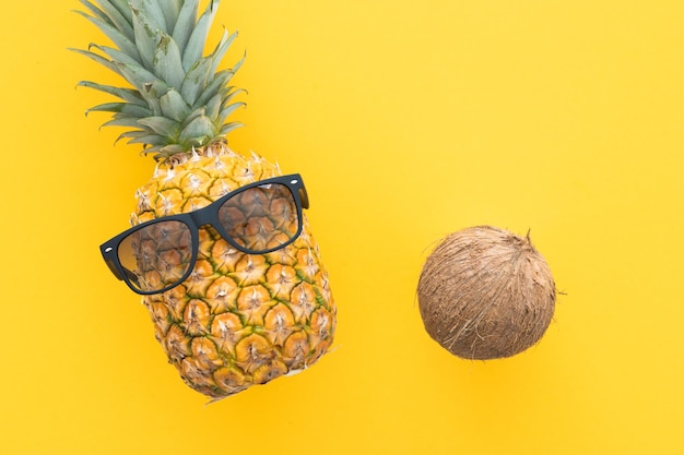Piña hipster y cocos con gafas de sol sobre un fondo amarillo