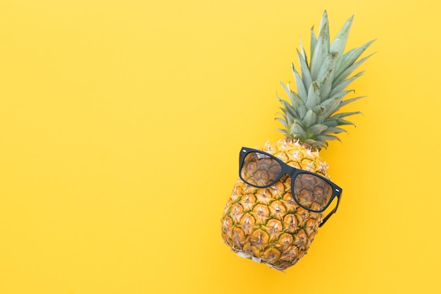 Piña hipster con gafas de sol sobre un fondo amarillo