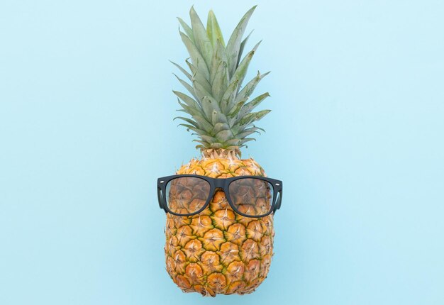 Piña hipster con gafas de sol sobre un fondo azul.