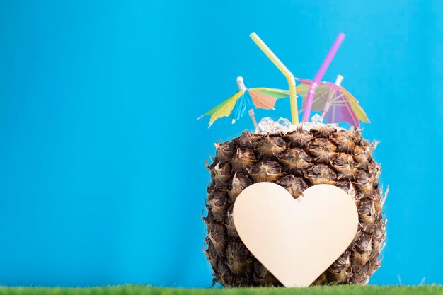 Piña jugosa en la hierba con un paraguas de hielo y un corazón para el día de san valentín en un fondo azul