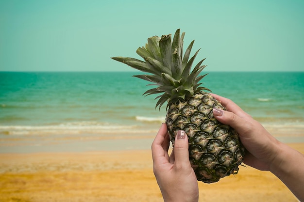 Piña madura en mano de mujer con playa tropical de fondo Concepto de verano tropical