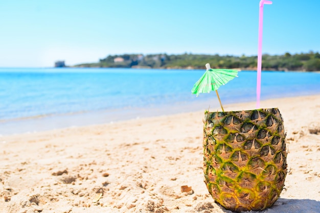 Piña con paja y sombrilla pequeña en la arena.