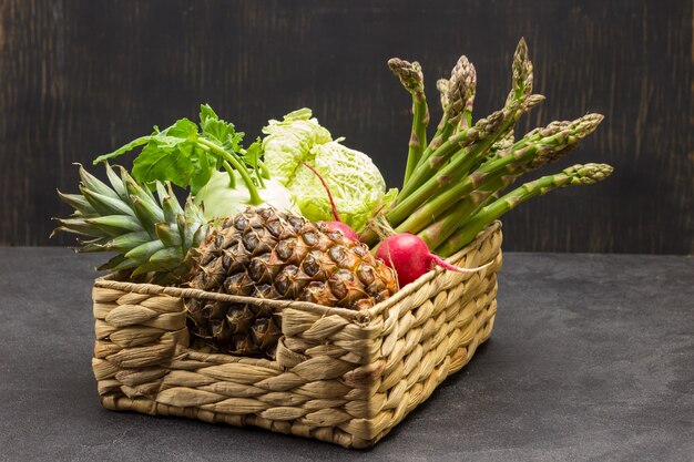 Piña y verduras en cesta de mimbre. Fondo negro. Copia espacio