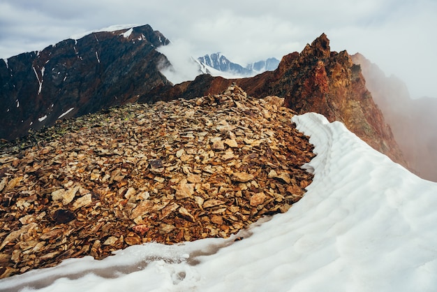 Pináculo rochoso pontudo bonito na montanha com neve entre nuvens baixas grossas. Paisagem alpina minimalista atmosférica. Topo da montanha rochosa afiada acima de nuvens espessas no abismo. Maravilhoso cenário das montanhas.