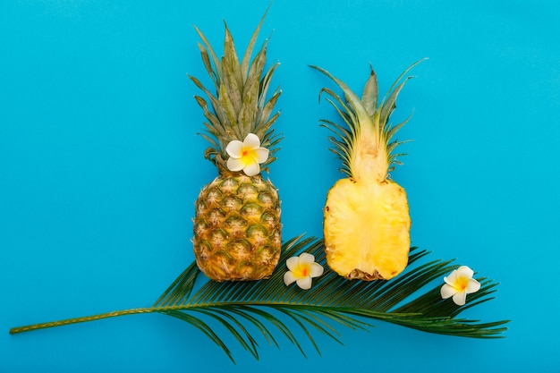 Piñas frutas de piñas de verano tropicales enteras y mitades de piña en rodajas con composición de flores de plumeria tropical sobre fondo de verano de color azul. Endecha plana. Foto de archivo de alta calidad