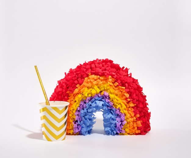 Una piñata de arco iris de colores brillantes y copas de vacaciones de papel con una pajita para varios cócteles y otras bebidas sobre un fondo blanco