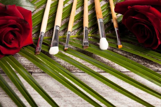 Pincéis de maquiagem ao lado de rosas em fundo de madeira