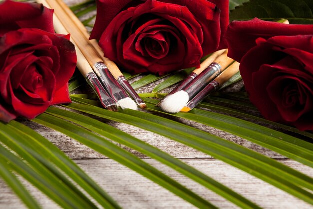 Pincéis de maquiagem ao lado de rosas em fundo de madeira