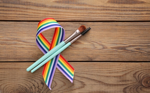 Pincéis de maquiagem com símbolo de fita de orgulho de arco-íris LGBT em fundo de madeira Vista superior