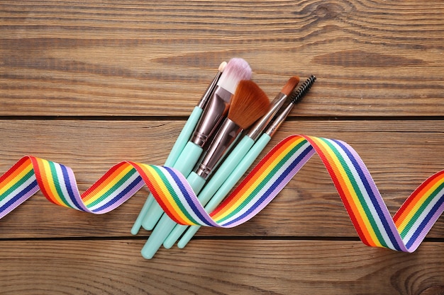 Pincéis de maquiagem com símbolo de fita de orgulho de arco-íris LGBT em fundo de madeira Vista superior