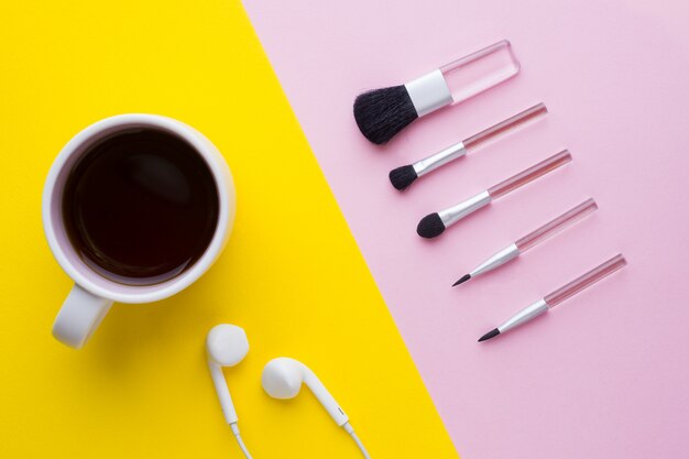 Pincéis de maquiagem em um fundo rosa pastel e uma xícara de café