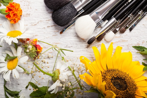 Pincéis de maquiagem em uma mesa ao lado de flores silvestres em fundo de madeira