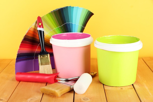 Pincéis de potes de tinta e amostras coloridas na mesa de madeira em fundo amarelo