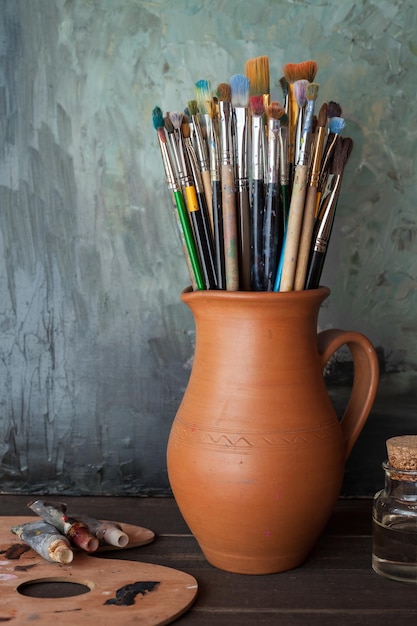 Pincéis em um jarro de tubos de tinta de paleta de argila de oleiro e garrafa de óleo no estúdio do artista