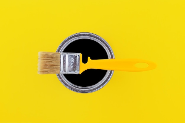 Pincel amarelo em uma lata aberta com tinta preta em uma vista superior de fundo amarelo