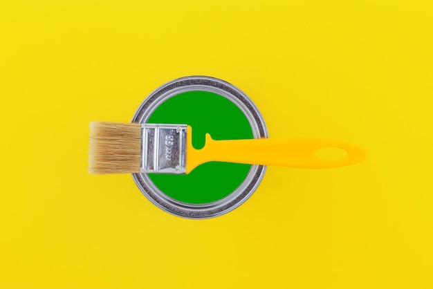 Pincel amarillo en una lata abierta con pintura verde sobre un fondo amarillo vista superior de primer plano