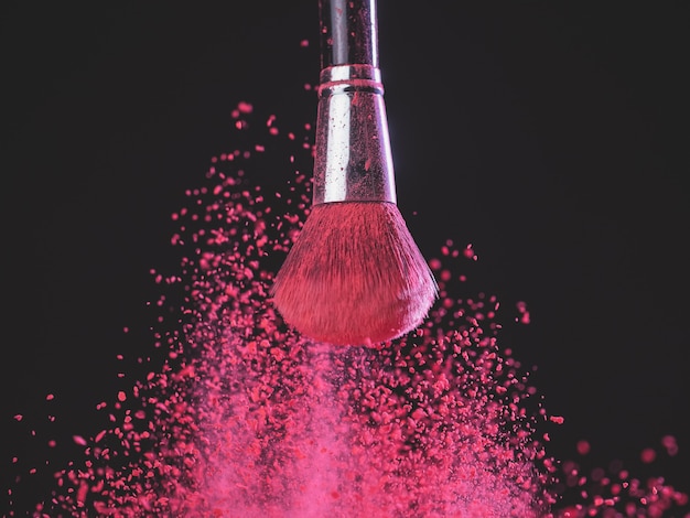 Pincel de maquiagem com explosão de pó rosa em fundo preto