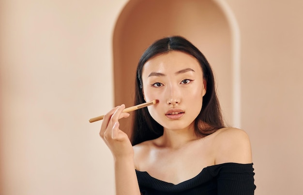 Pincel de maquiagem Jovem mulher asiática séria em pé dentro de casa