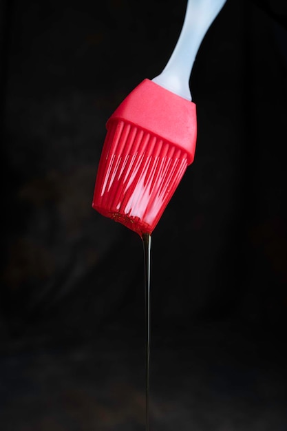 Pincel de silicone para cozinhar vermelho com óleo pingando em um fundo escuro