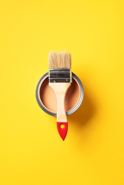 Pincel e lata de tinta aberta com fundo amarelo da moda Espaço de cópia de vista superior Edifício de reparo de renovação de apartamento e conceito de design de casa