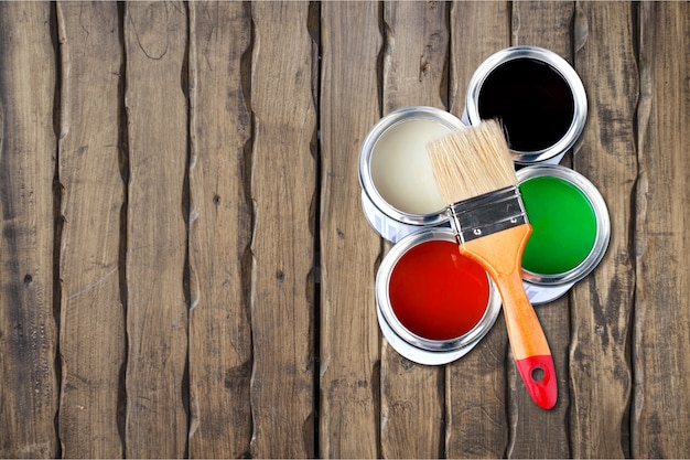 Pincel y latas de pintura para reparar sobre fondo de madera