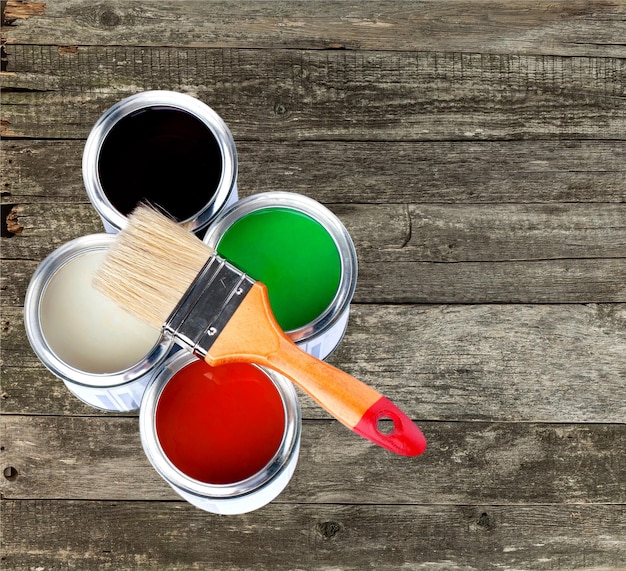 Pincel y latas de pintura para reparar sobre fondo de madera