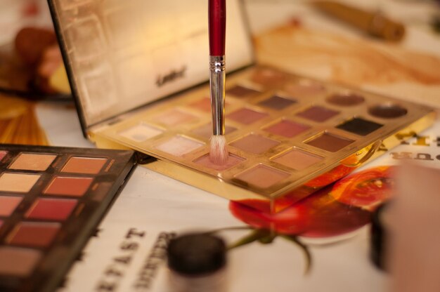 Un pincel de maquillaje con una pila blanca se sumerge en una paleta con sombras en el fondo de los cosméticos.