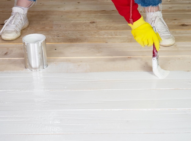 Pincel con pintura blanca en la mano de una chica de cerca, la chica pinta una superficie de madera