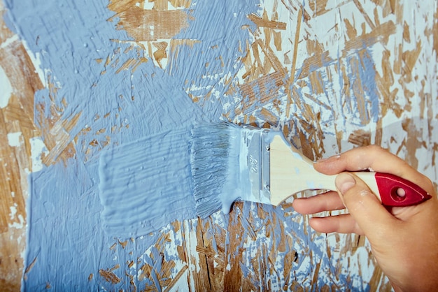 Pincel de pintura en la mano del trabajador de la construcción El pintor de la casa aplica pinceladas con pintura gris a la pared de chapa