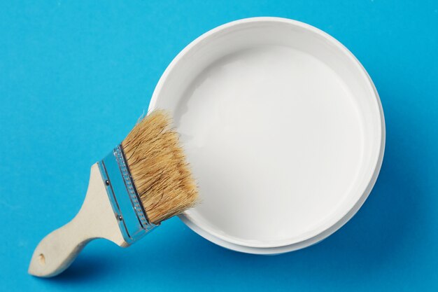 Pincel y pintura puede con color blanco sobre un fondo azul, primer plano