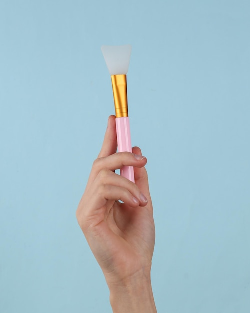 Pincel de plástico de maquillaje en mano femenina sobre un fondo azul