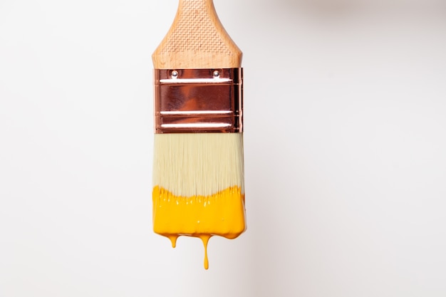 Pincel de primer plano con pintura amarilla líquida gotea del pincel
