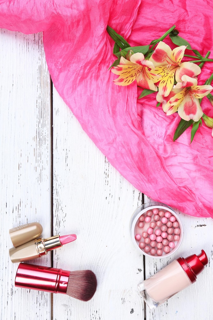 Foto pincel de sombra de ojos, pintalabios y flores sobre fondo de madera de color