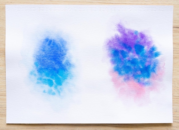 Pinceladas coloridas de aquarela na folha de papel branco com fundo de madeira Closeup